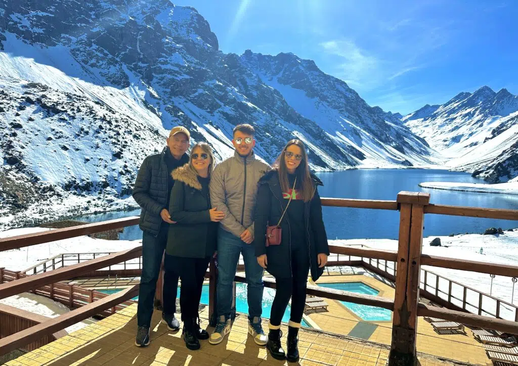 Grupo de quatro pessoas em passeio perto de Santiago posando em um mirante em Portillo, com a Laguna del Inca ao fundo e montanhas nevadas da Cordilheira dos Andes sob céu azul.